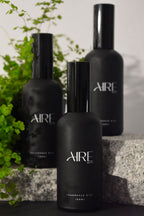 Three black Aire & Co home fragrance bottles on a stone surface with greenery in the background.