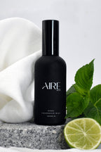 Linen Aire & Co home fragrance mist bottle with green leaves, white fabric and a lime on a gray stone.