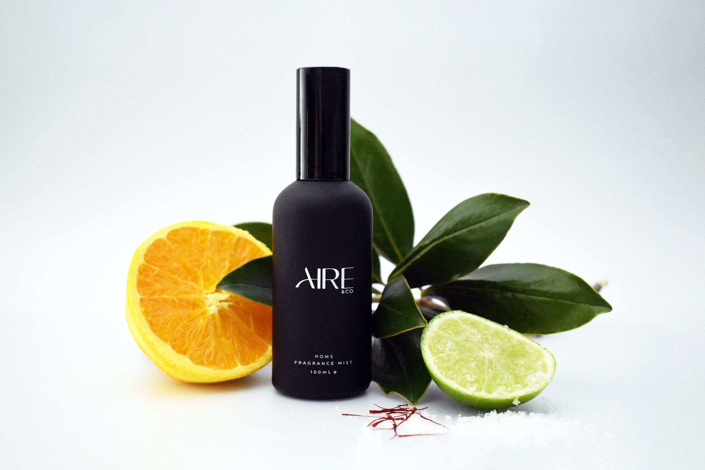 Ocean Aire & Co home fragrance mist bottle with an orange slice, a lime slice,  rock salt and green leaves on a white background