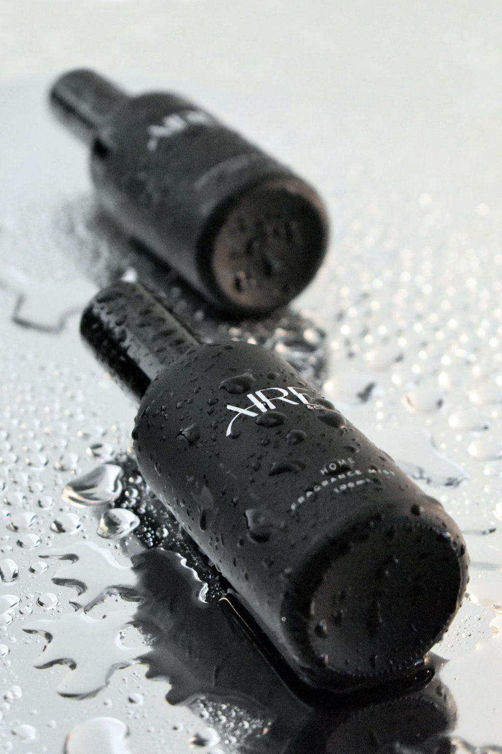Two black ocean Aire & Co home fragrance mist bottles on a wet surface