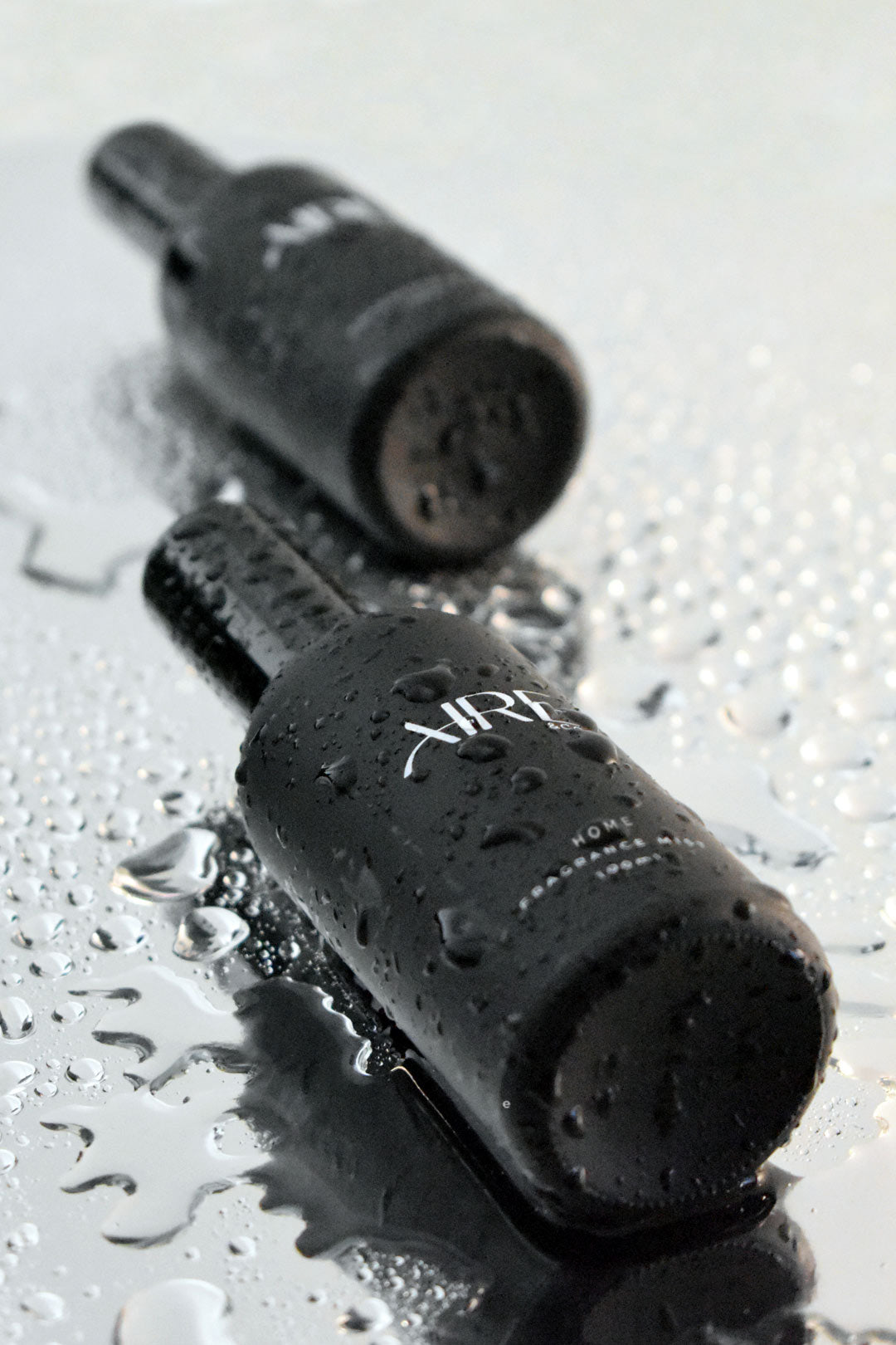 Two black ocean Aire & Co home fragrance mist bottles on a wet surface