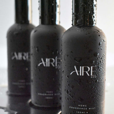 Three black bottles of Aire & Co home fragrance mist with water droplets on a reflective surface.