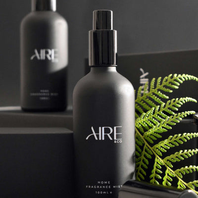 Two black Aire & Co home fragrance mist bottles with a fern leaf on a dark background