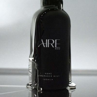 Wet black Aire & Co home fragrance mist on a reflective surface with a gray background